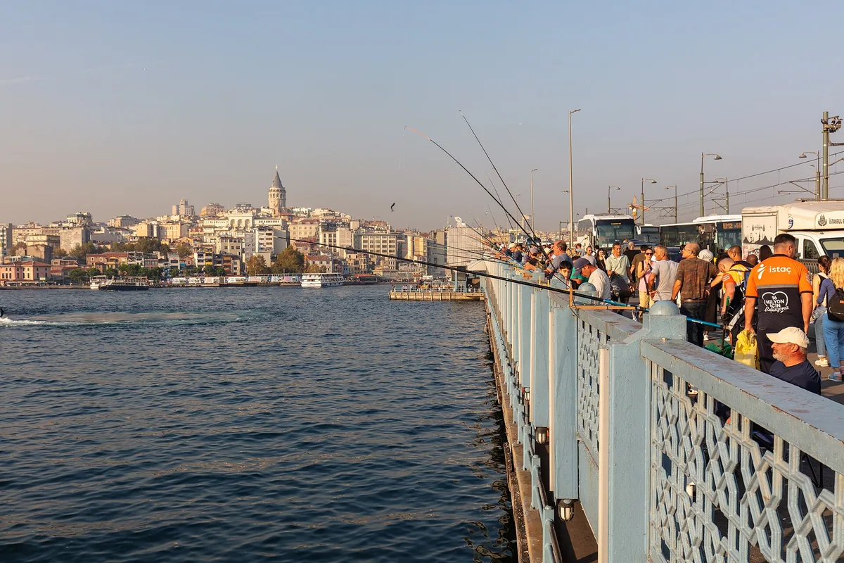 Fiskare längs räcket på Galatabron, med Galata-kullen och dess torn i fjärran över vattnet.