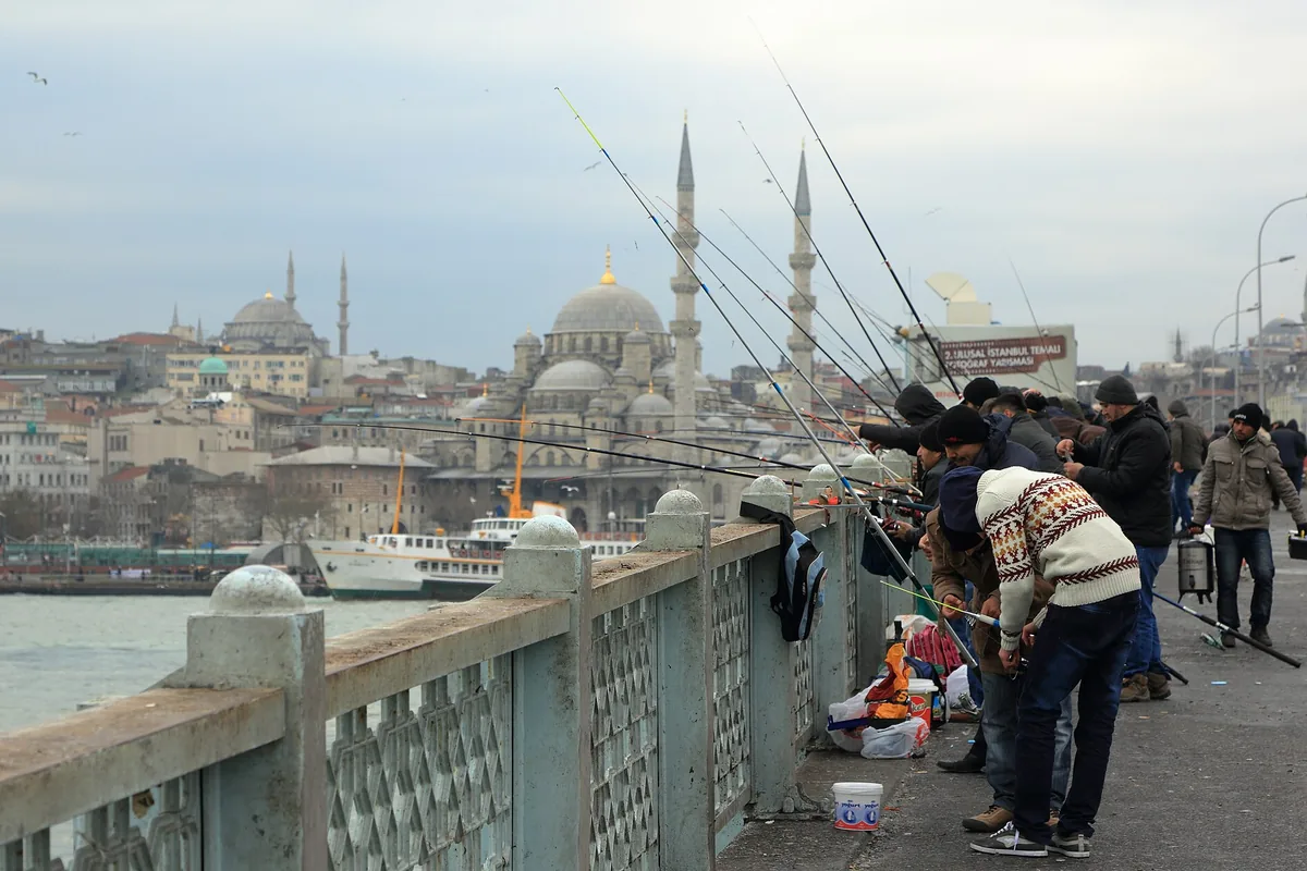Fiskare längs räcket på Galatabron, med gamla stadens kupoler och minareter bakom sig.
