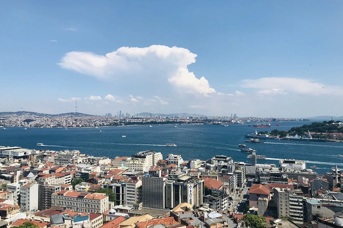 Utsikten över Beyoğlus hustak mot Gyllene hornet, Bosporen och den bortre stranden under en molnig blå himmel.